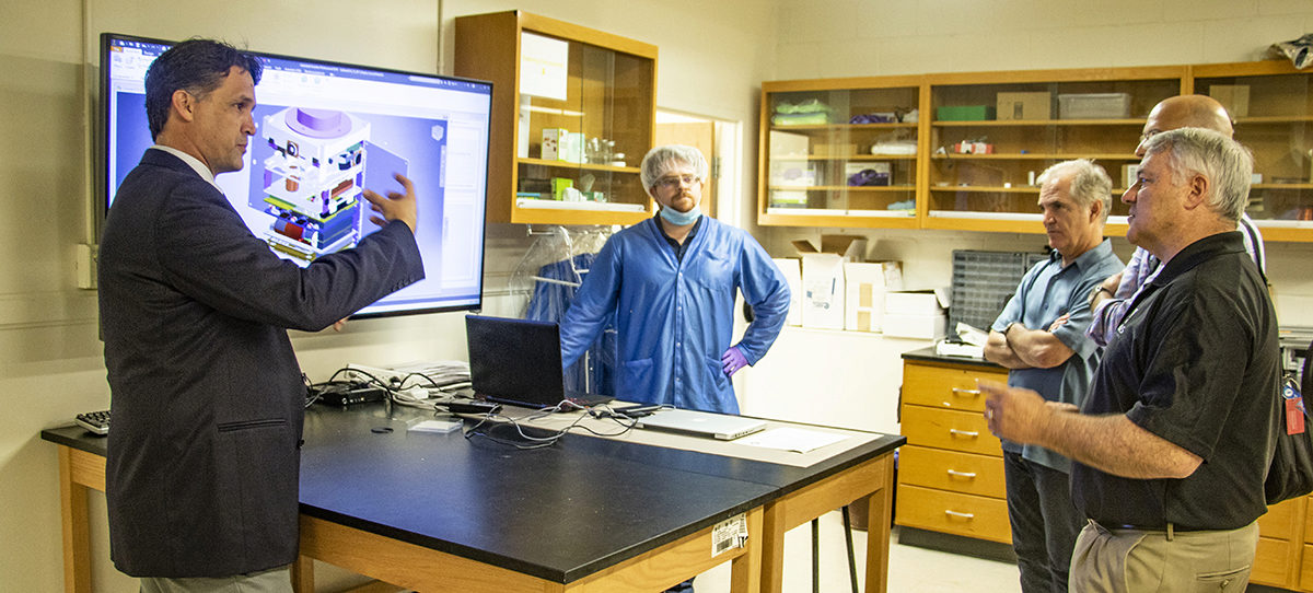 Prof. Brian Gunter standing next to a computer screen explaining his work to four representatives from Xenesi