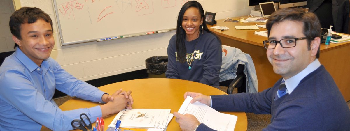 Prof. Julian Rimoli sitting at a table talking with two of his students