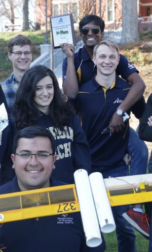 Students grouped together with a first place plaque and with one of the winning aircraft